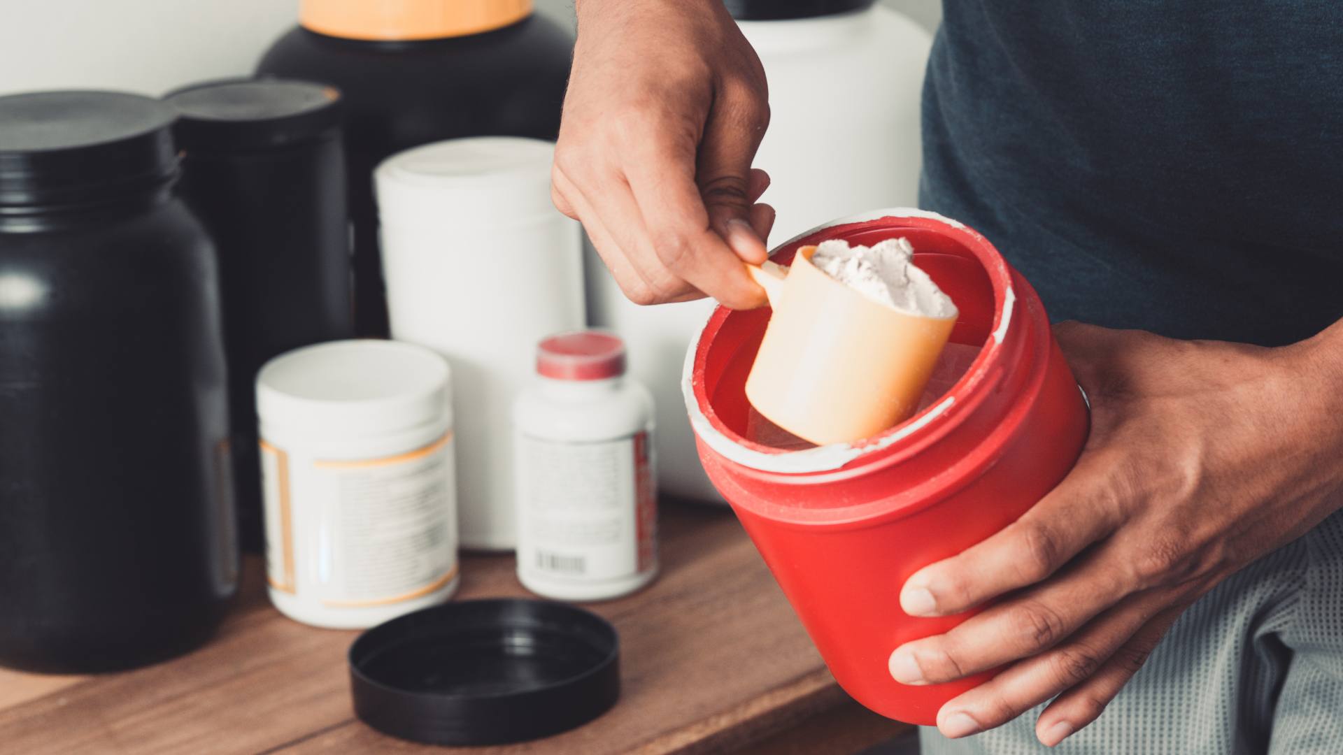 A person scoops creatine out of a red container.