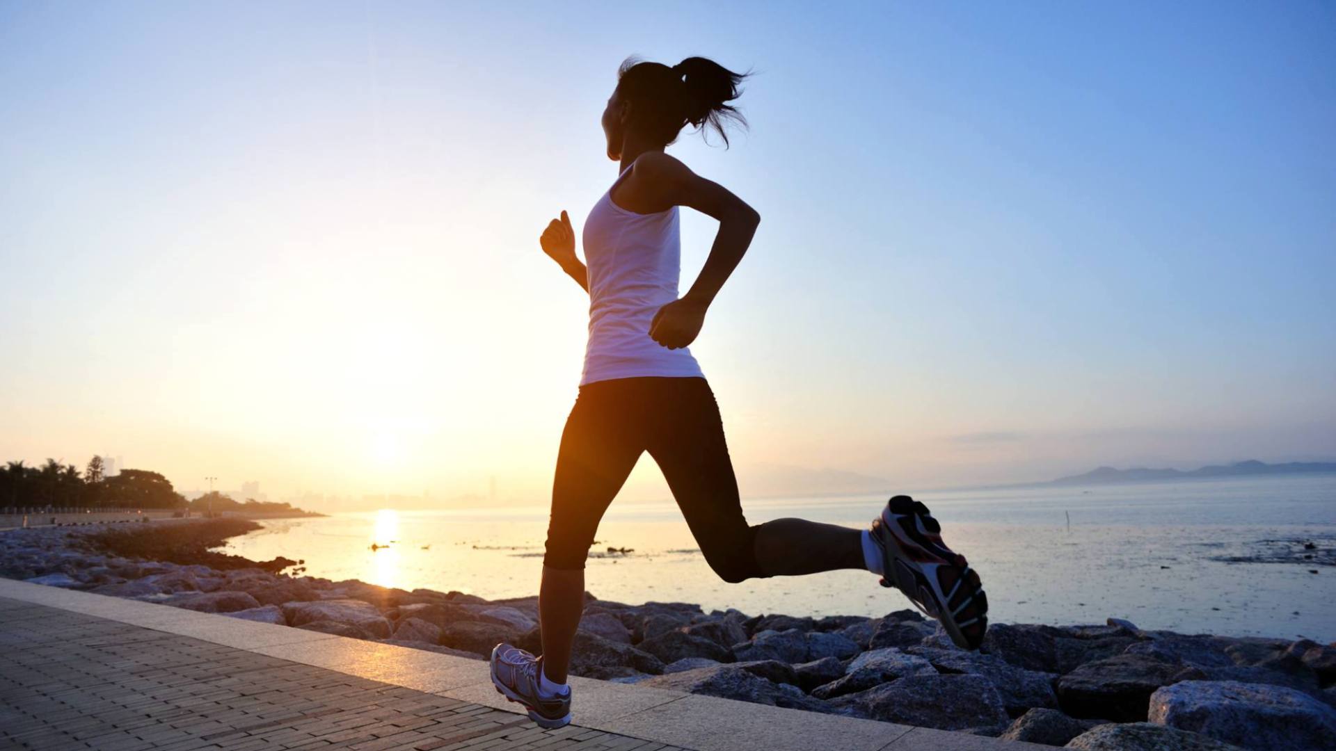 A woman runs outside next to water, demonstrating healthy lifestyle interventions.